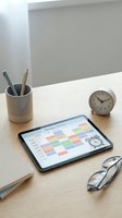 Modern workspace with tablet displaying weekly schedule calendar app on wooden desk with clock and office supplies for productivity planning.