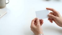 Close-up of two hands holding blank white business card on clean desk with coffee cup, suitable for branding and corporate identity mockups.