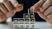 Businessman hands protecting wooden blocks with 1% symbols arranged in pyramid formation representing gradual growth and financial planning strategy.