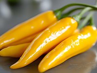 Fresh yellow chili peppers with bright glossy skin and green stems on dark surface, macro food photography showing texture and natural shine.