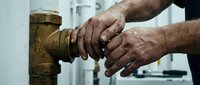 Professional plumber hands installing brass pipe fitting with wrench in modern bathroom renovation project for home improvement services.