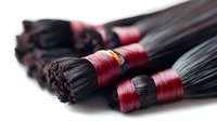 Black hair extensions tied with red thread on white background, professional hairdressing supplies for salon use, beauty industry equipment macro photography.
