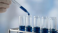Laboratory scientist using pipette to transfer blue chemical solution into glass test tubes for research experiment and analysis in modern lab setting.