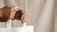 Close-up of male hands holding white cotton tote bag against neutral background. Suitable for eco-friendly shopping, sustainable lifestyle, retail, and branding campaigns.