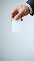 Mature male professional in dark business suit holding blank white card with fingers, isolated on neutral background for corporate branding and business messaging applications.