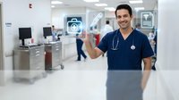 Young Hispanic male doctor in navy scrubs touching digital healthcare interface icon in modern hospital setting with medical equipment and technology.
