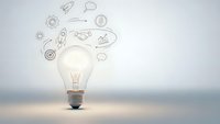 Glowing light bulb with creative business icons and symbols floating above representing innovation, brainstorming and entrepreneurial ideas for startup success.