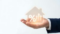 Businessman hand holding glowing house icon with percentage symbol representing mortgage rates, real estate investment and property financing concepts.