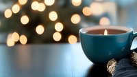 Cozy winter evening with glowing candle in blue ceramic cup against blurred Christmas lights background, knitted texture and ornament decoration.