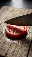 Sliced ripe tomato on rustic wooden cutting board with chef knife, fresh produce for cooking and food preparation.