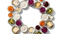 Colorful assorted dips and spreads arranged in circular pattern on white background. Various sauces including hummus, beetroot, cheese for party appetizers.