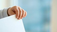 Newborn baby hand grasping white paper against soft blue blurred background, symbolizing new life, innocence, and parenting concepts for healthcare and family-related projects.