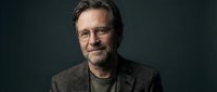 Mature Caucasian businessman with glasses and beard smiling confidently in professional portrait against dark background for corporate marketing materials.