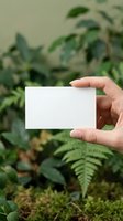 Hand holding blank white business card mockup against natural green plant background for branding and corporate identity design projects.