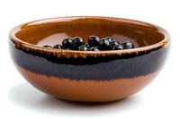 Fresh blueberries in rustic ceramic bowl with two-tone brown and black glazed finish on white background, isolated for easy design integration.