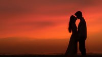 Romantic couple silhouette embracing at sunset with dramatic orange sky and mountain landscape creating intimate moment for love and relationship concepts.