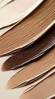 Smooth textured strokes of liquid foundation in various nude and brown shades creating abstract pattern on light background. Cosmetic product texture close up.