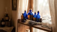 Vintage blue glass bottles with lavender sprigs and sea salt on rustic wooden shelf by window. Apothecary style home decor for natural wellness and aromatherapy.