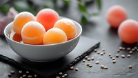 Fresh organic peaches in white ceramic bowl on rustic wooden table with scattered coffee beans and green foliage background for healthy eating concepts.