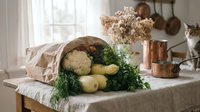Rustic kitchen scene with fresh vegetables spilling from a paper bag on a wooden table, copper pots, dried flowers, and a curious cat nearby.