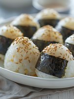 Japanese rice balls onigiri with nori seaweed and sesame seeds served on white plate. Traditional Asian cuisine close up view with selective focus.
