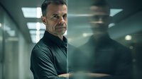 Mature Caucasian man in black shirt standing in dark office corridor with dramatic lighting and reflection. Professional corporate environment portrays confidence and authority.