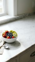 Assorted fresh fruits including strawberries, blueberries, and kiwi slices arranged in white bowl on marble kitchen countertop near window with natural light for healthy eating and nutrition content.