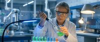 Senior Asian male scientist in white lab coat and safety glasses conducting chemical experiment with test tubes and pipette in modern research laboratory.