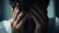 Man with hands covering face expressing intense emotional distress, anxiety, or grief in dimly lit setting, conveying mental health struggle.
