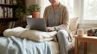 Young woman working on laptop computer from home sitting on comfortable sofa in cozy living room with books and plants creating productive workspace atmosphere.