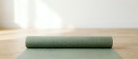 Rolled green yoga mat on wooden floor with natural sunlight, ready for fitness and wellness practice sessions.