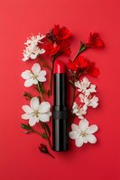 Red lipstick with white spring blossoms and red flowers arranged on vibrant coral background. Flat lay cosmetic composition for beauty and makeup advertising.