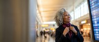 Mature African American businesswoman adjusting tie in modern airport terminal with departure board, professional travel concept for corporate presentations.
