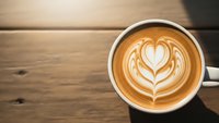 Coffee cup with heart latte art on wooden table. Barista crafted cappuccino with milk foam design for cafe menu, morning beverage and coffee shop branding.