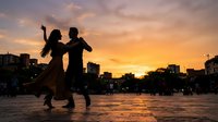 Silhouetted couple dancing together in urban plaza at golden sunset, creating romantic atmosphere for lifestyle and relationship content.