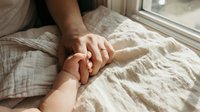 Tender moment of adult and baby hands touching on soft white bedding near a window, symbolizing love, care, and family bond.