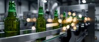 Green beer bottles on industrial production line with bokeh factory lights in background, manufacturing and beverage industry concept.