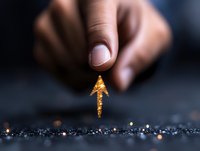 Glowing golden arrow floating between fingers against dark background with sparkles, representing business growth, success and direction concept.