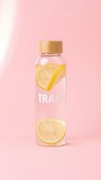 Clear glass water bottle with wooden bamboo cap containing fresh lemon slices and infused water against soft pink background. Refreshing beverage for hydration and wellness.