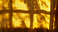 Warm sunlight streaming through window creates dramatic shadow patterns on textured linen curtain, casting golden hour glow and geometric shapes for atmospheric mood.
