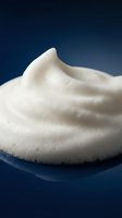Creamy white foam texture with smooth swirls and bubbles on dark blue background for skincare and cosmetic product applications.