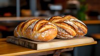Fresh artisanal sourdough bread loaves with crispy golden crust arranged on wooden cutting board, showcasing rustic bakery products with natural lighting.