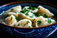 Homemade dumplings with fresh parsley in traditional blue and white ceramic bowl. Close up view of steaming hot Asian cuisine garnished with herbs.