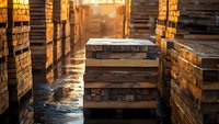 Stacked wooden planks and lumber materials in industrial warehouse with warm sunlight creating atmospheric lighting for construction projects.