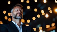 Confident mature Caucasian businessman with gray beard wearing suit against blurred bokeh lights background, looking up thoughtfully in evening atmosphere.