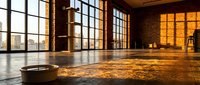 Spacious industrial loft with large windows, polished concrete floors, and warm golden sunlight streaming through glass panes, suitable for events, studios, or commercial spaces.
