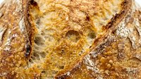 Freshly baked artisan bread with crispy golden crust and flour dusting, showcasing rustic texture and traditional baking techniques for bakery and food photography.