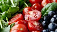 Fresh mixed salad with cherry tomatoes, blueberries and spinach leaves on white background. Healthy organic vegetables and berries for cooking and nutrition.