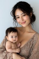Young Asian mother in lace dress holding adorable baby against white background, intimate maternal bonding moment captured in soft natural lighting.