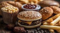 Juicy cheeseburger with sesame seed bun alongside golden french fries and chocolate desserts on rustic wooden table, fast food restaurant menu composition.
